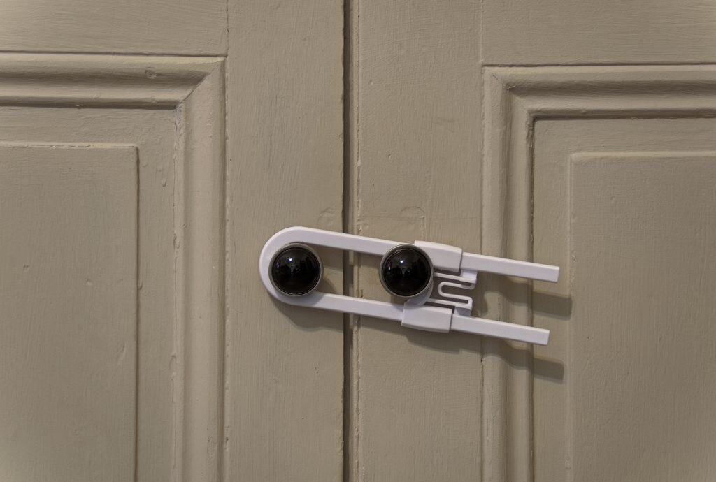 Close up view of a white child safety lock holding two cabinet doors together