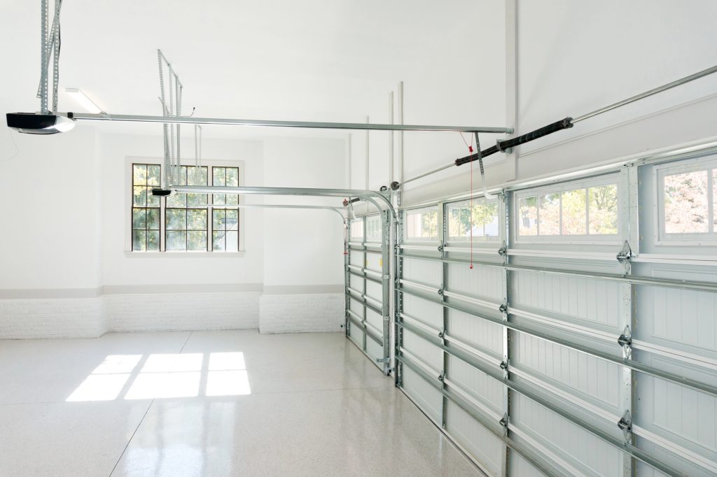 Clean, bright garage interior with white walls, polished concrete floors, and modern sectional doors featuring transom windows that flood the space with natural light.