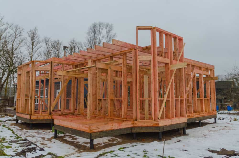 A modern timber-framed house takes shape amidst a snowy landscape, showcasing the beauty of construction in progress.