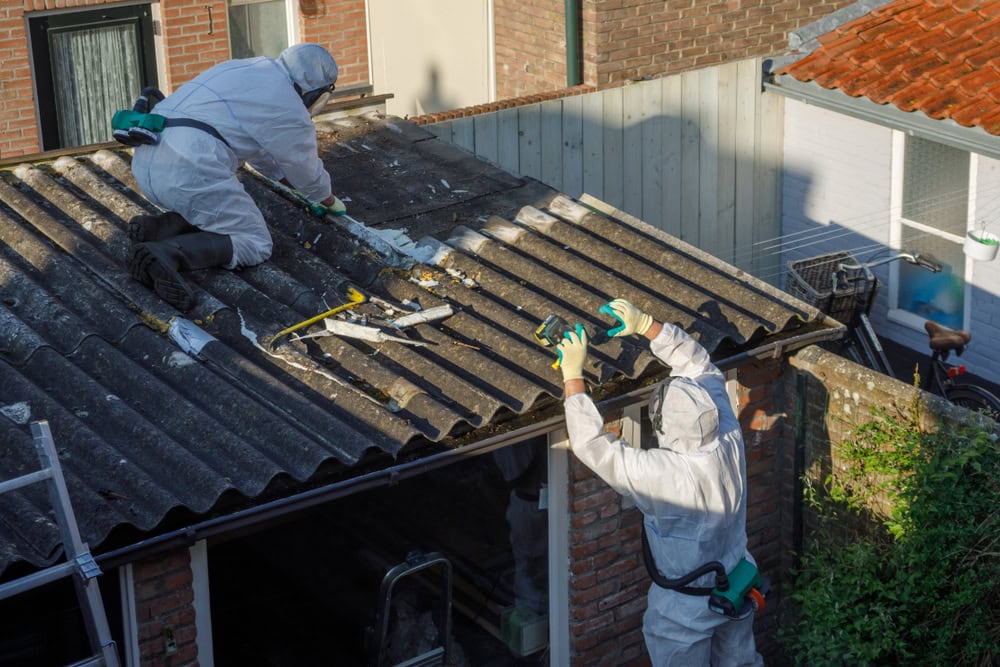 Workers in protective suits safely remove asbestos roofing.