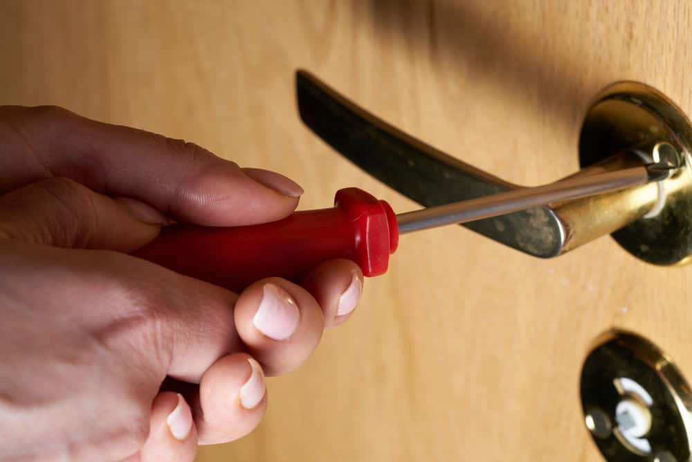 Close-up of hands using a screwdriver to tamper with a door lock.