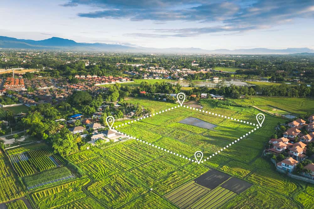 Prime real estate outlined amidst lush green rice fields and suburban homes, with scenic mountains in the distance.
