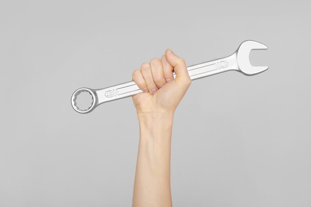 A hand holding up a silver combination wrench against a gray background