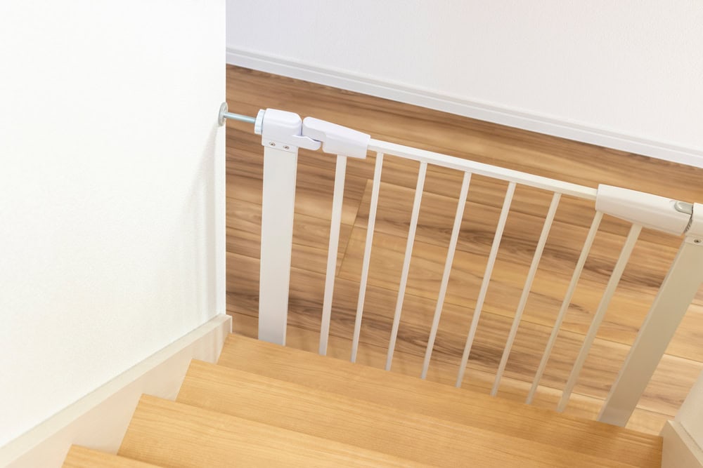A baby gate secures the top of wooden stairs in a modern home.