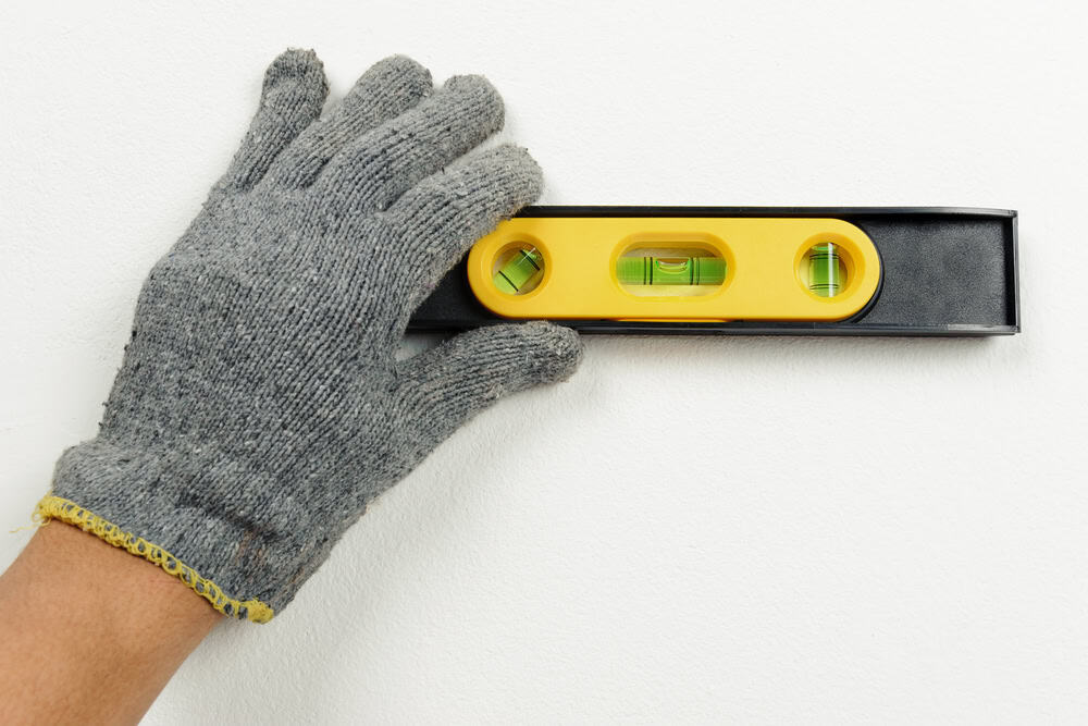 A gloved hand holds a spirit level against a wall, ensuring precision in construction work.