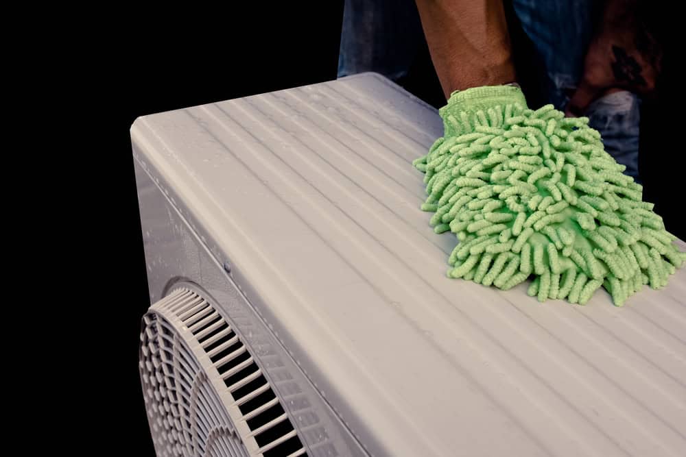 Cleaning the AC unit with a microfiber glove for a fresh and cool environment.