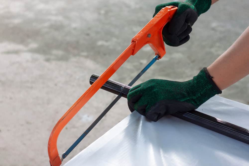 Worker using a hacksaw to cut a metal pipe, wearing protective gloves for safety.