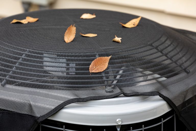 Fallen autumn leaves rest on a mesh-covered outdoor AC unit.