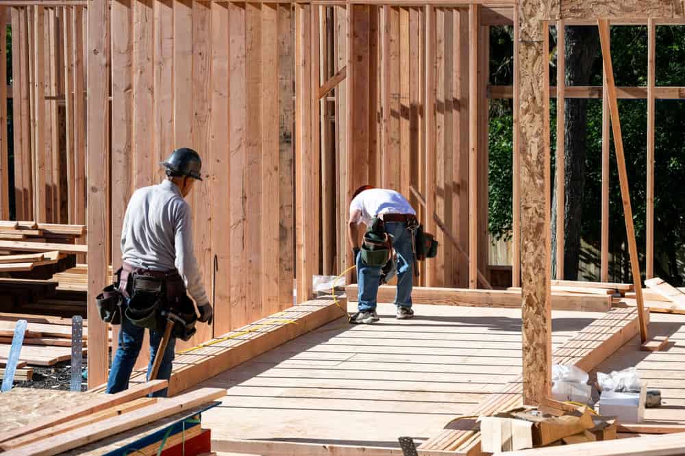 Two construction workers diligently work on framing a house, surrounded by wood and tools.