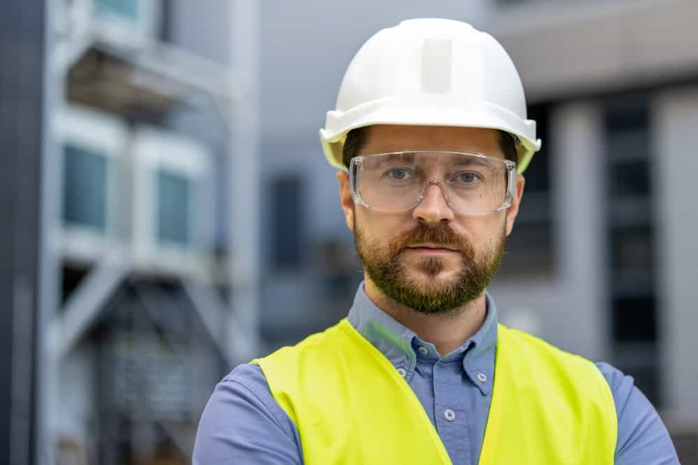 A construction worker stands confidently on site, equipped with safety gear.