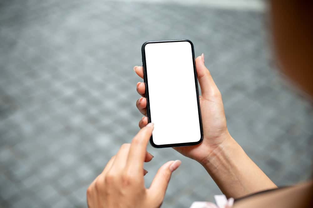 A hand holding a smartphone with a blank white screen while another finger hovers above it, poised to tap.