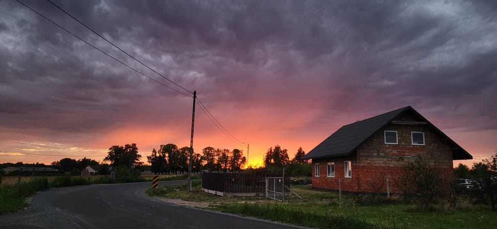 Fiery sunset casts a warm glow over a quiet countryside road and rustic brick house.