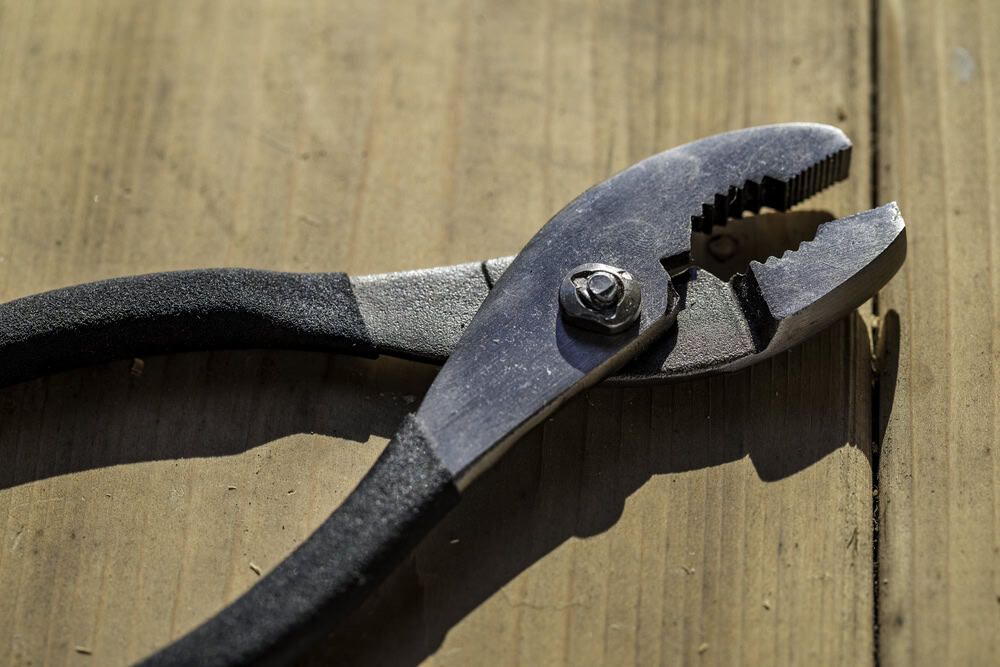 A sturdy pair of pliers ready for any task on a sunlit wooden surface.