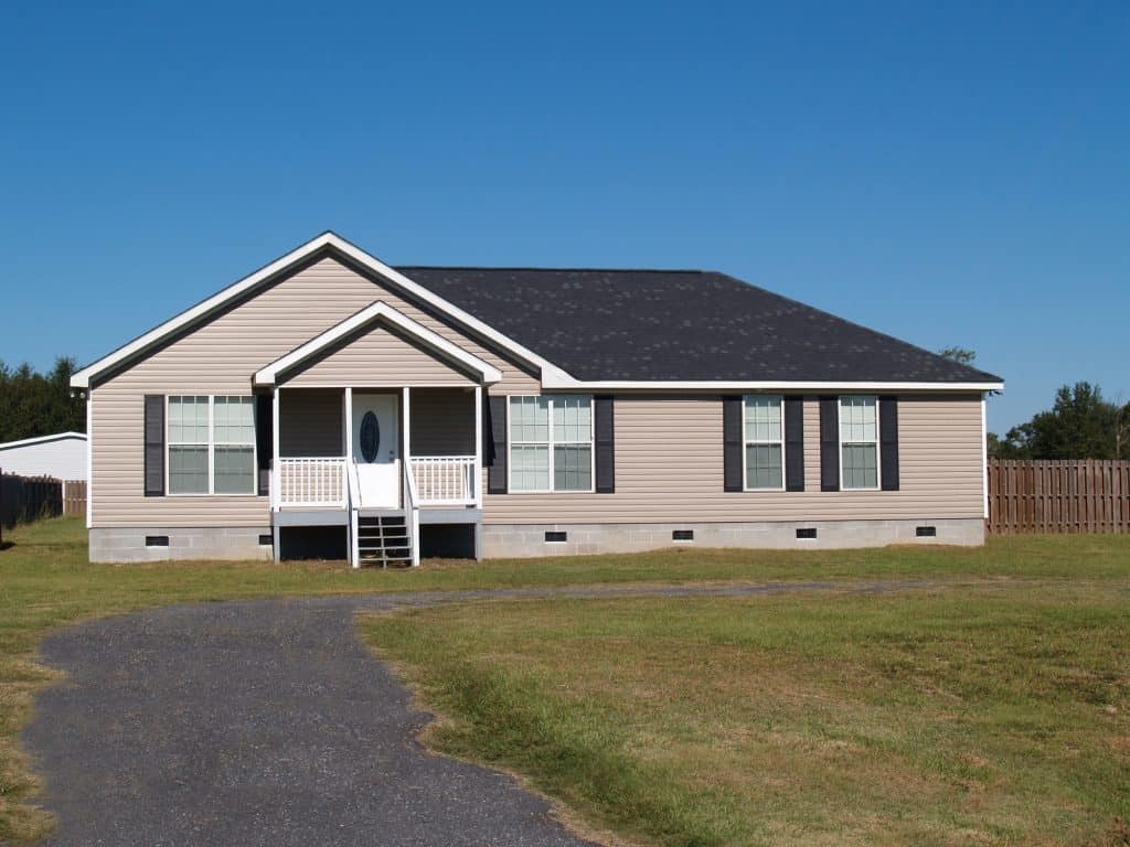 A charming suburban home with a welcoming front porch and a spacious yard under a clear blue sky.