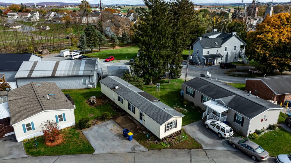 A quaint neighborhood with a mix of houses and mobile homes, surrounded by lush greenery and fall foliage.