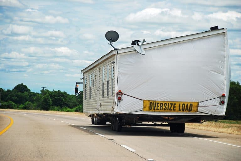 A massive mobile home labeled "OVERSIZE LOAD" travels down a highway.