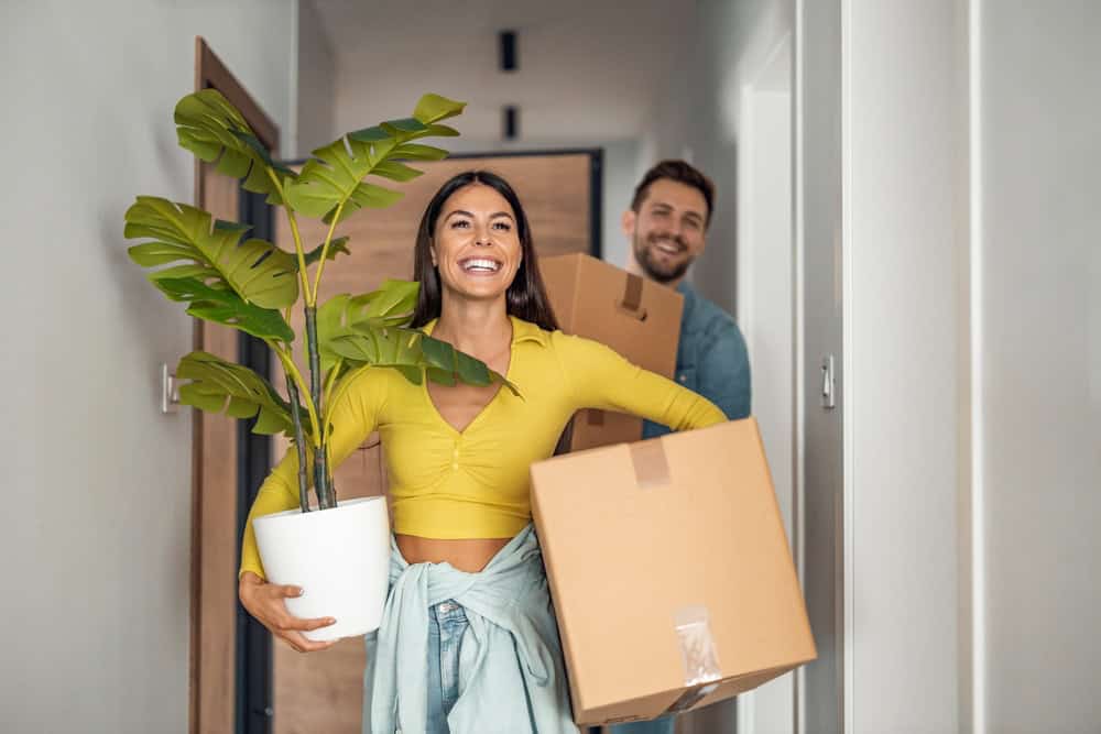 Excited couple moving into their new home, arms full of boxes.