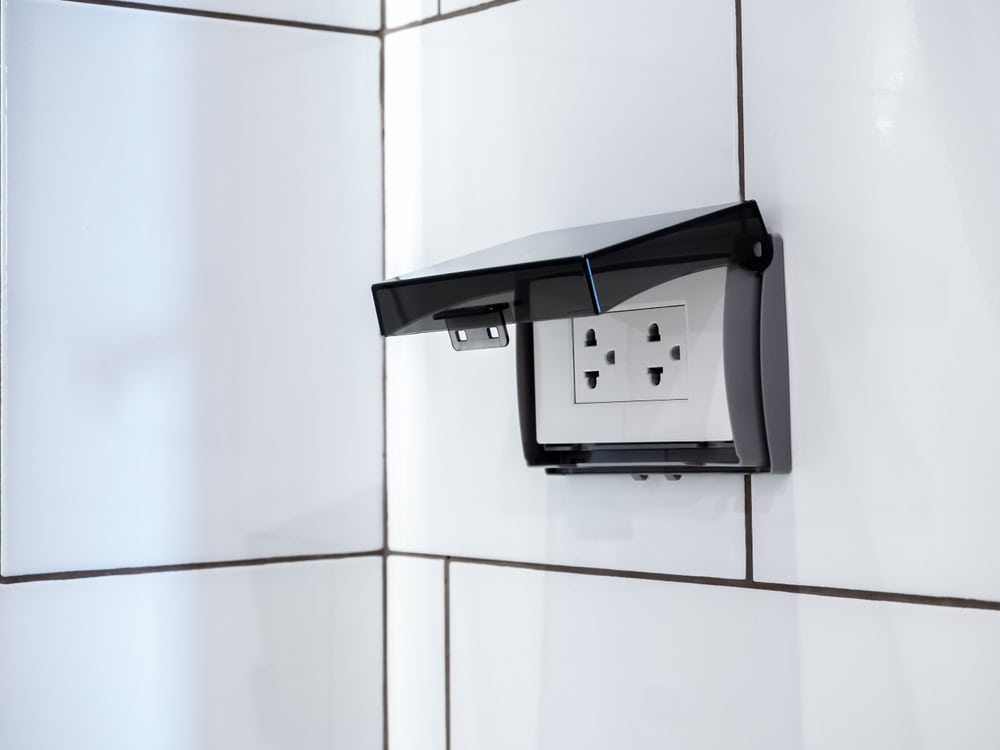 Modern waterproof electrical outlet with protective cover installed on a tiled wall.