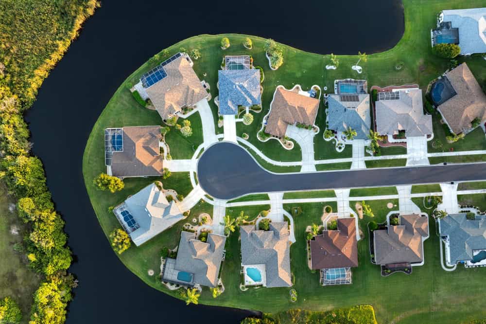 Aerial view of a picturesque neighborhood with sprawling homes, lush green lawns, and serene water views.