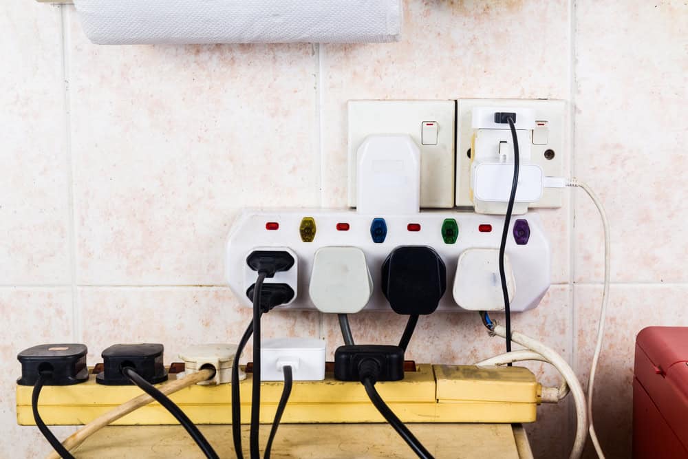 Dangerous overload: multiple electrical plugs crammed into extension sockets in a kitchen wall outlet.