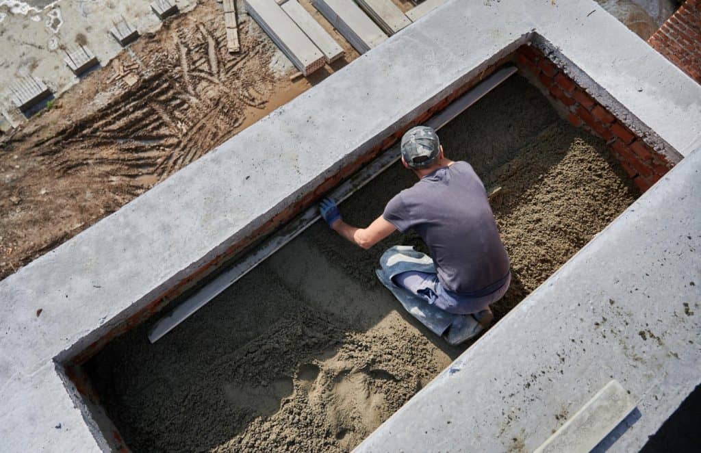 Construction worker smoothing fresh concrete in a basement foundation, using a screed board to create a level surface.