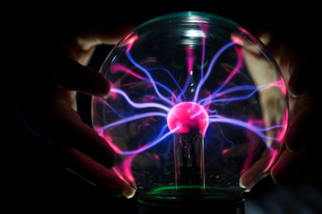 Electric energy dances across a plasma ball, with vibrant pink and blue tendrils of light reaching out from its glowing core, creating a mesmerizing display against the darkness.