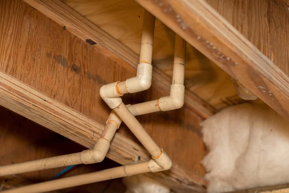 PVC pipes navigate through the wooden beams of a crawlspace.