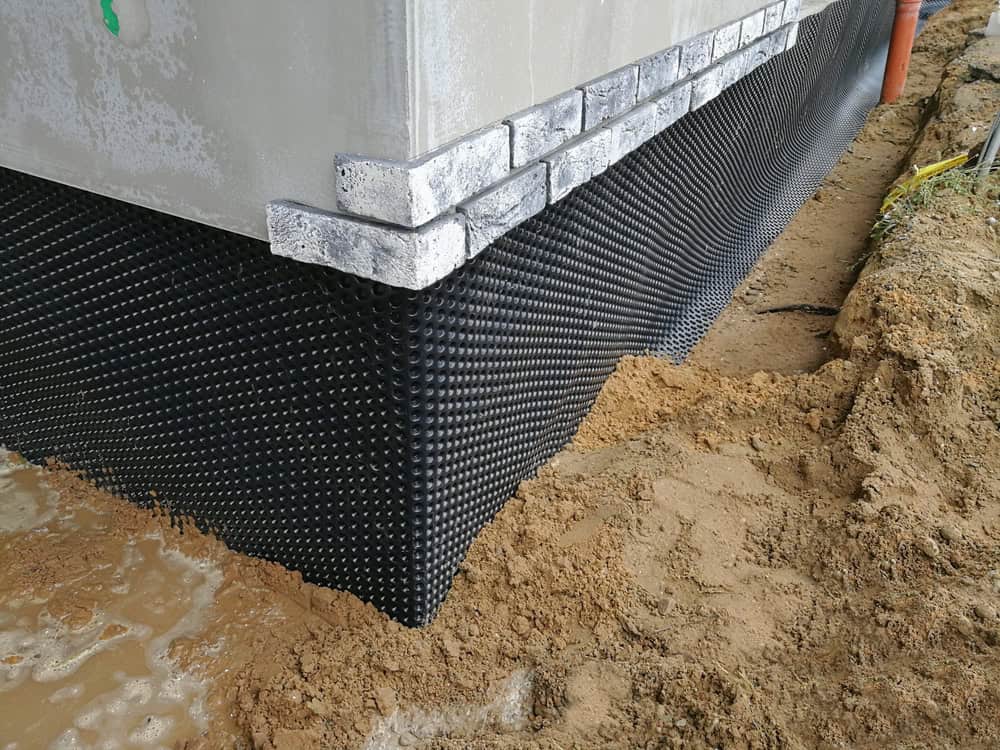 Foundation waterproofing in progress with dimpled membrane protecting the basement wall from moisture and soil.