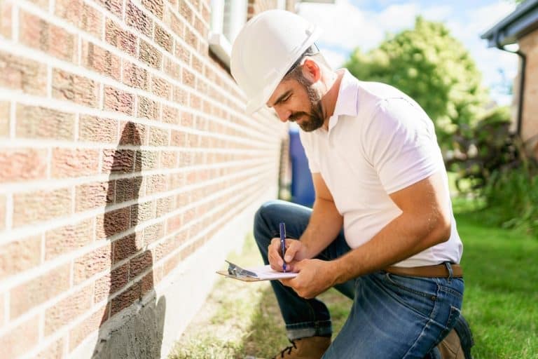 Home inspector evaluates brick foundation, documenting findings on a sunny day.