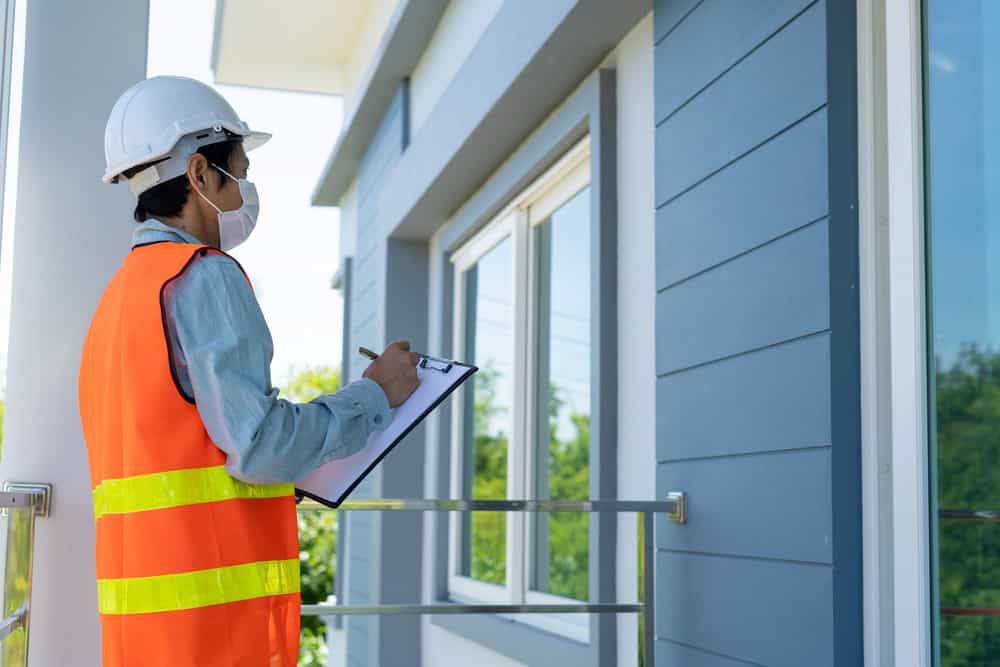 Inspector in safety gear evaluates a modern home's exterior during a routine site assessment.