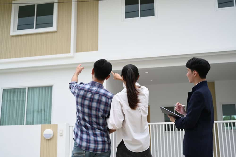 Three people inspecting a house exterior, with one pointing and another taking notes on a clipboard.