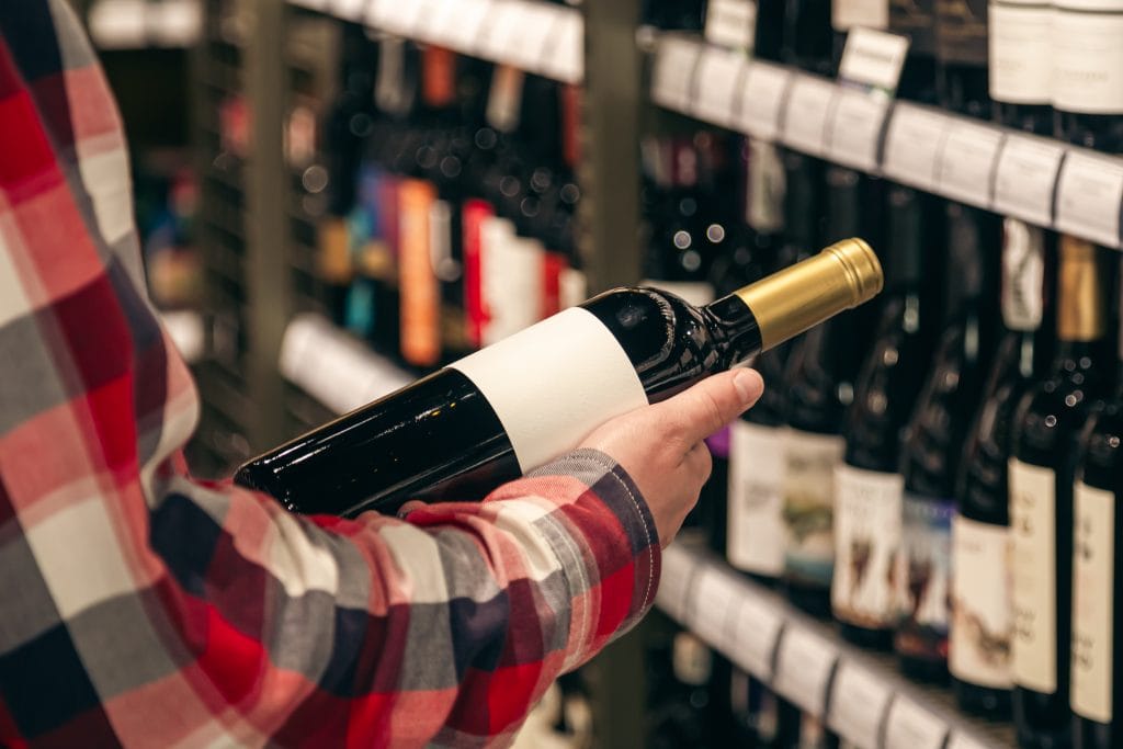 A man holding a wine bottle in a liquor wine shop, choosing the right wine from all the variations of wine bottles on the shelves.