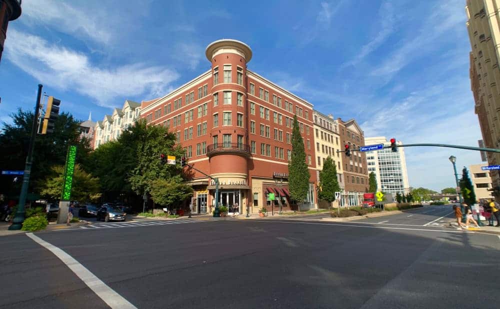 Historic brick building anchors this vibrant urban corner in downtown, featuring distinctive circular architecture and street-level retail beneath blue summer skies.