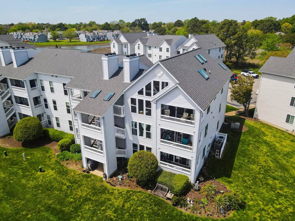 A serene view of modern condo nestled in a lush, green community with a picturesque lake in the background.
