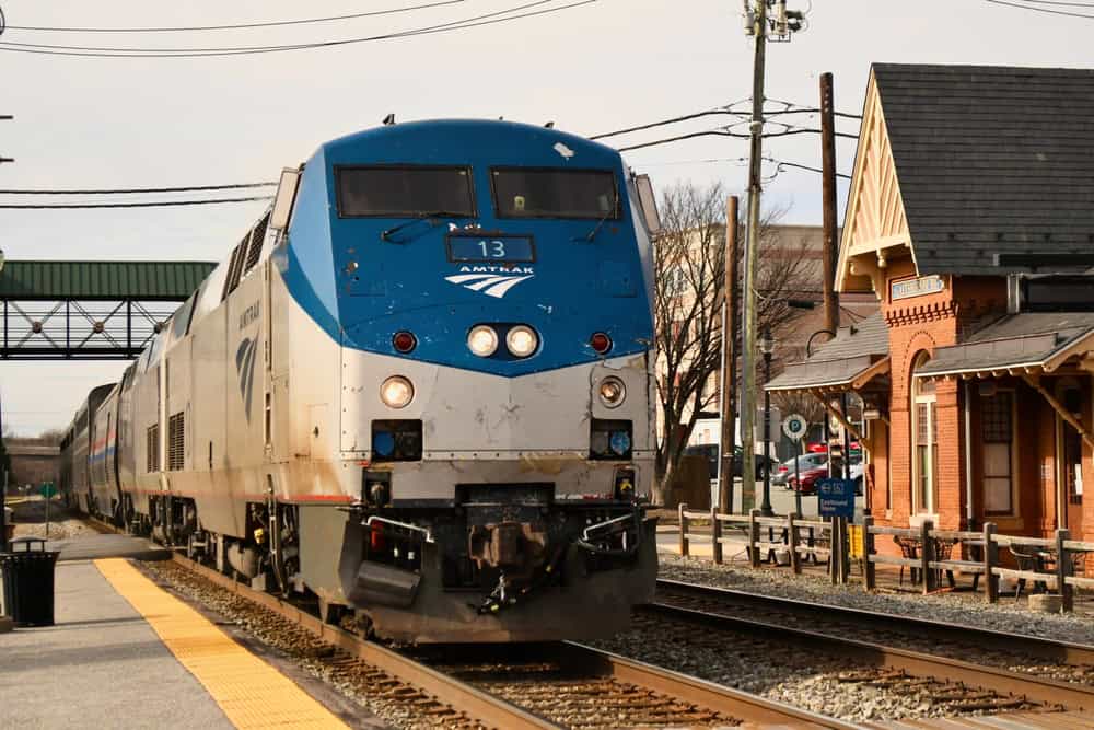 A sleek Amtrak train, numbered 13, rolls into a quaint, historic station under a clear sky.