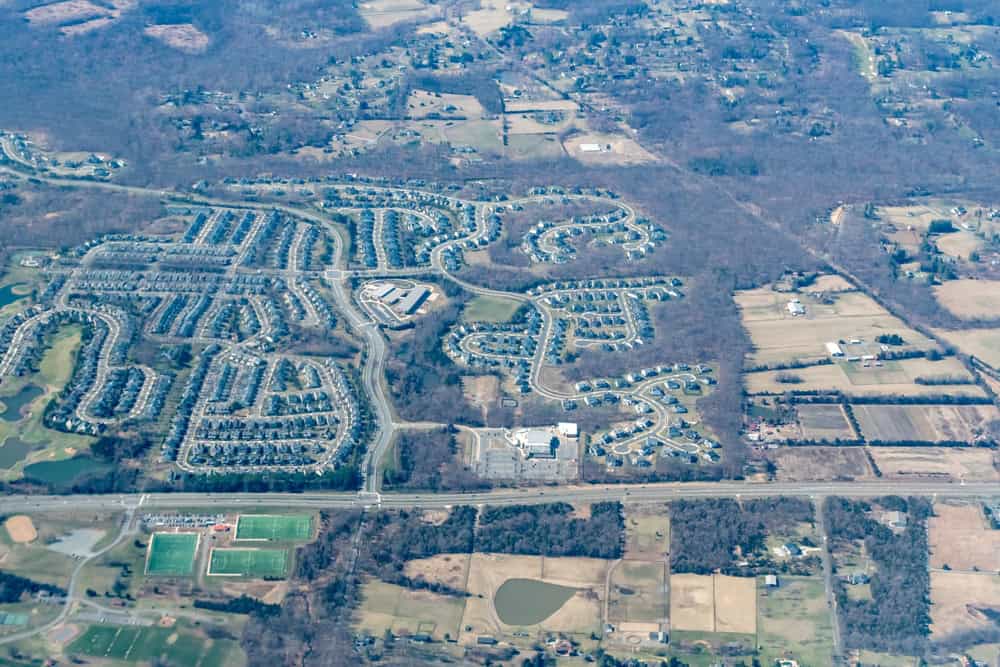 Aerial view of a sprawling suburban neighborhood bordered by farmland and sports fields.