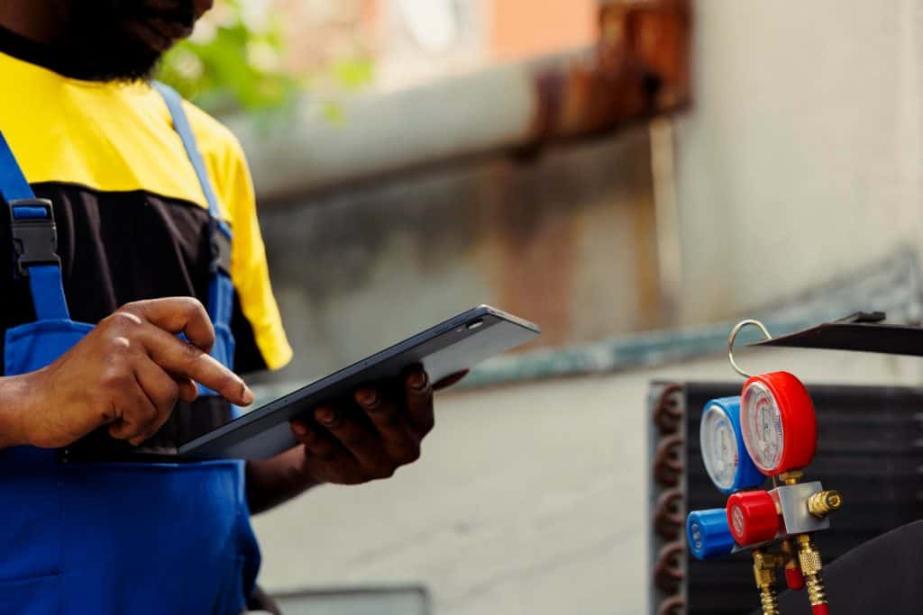 HVAC technician checks digital readings while servicing equipment, with pressure gauges visible in the foreground
