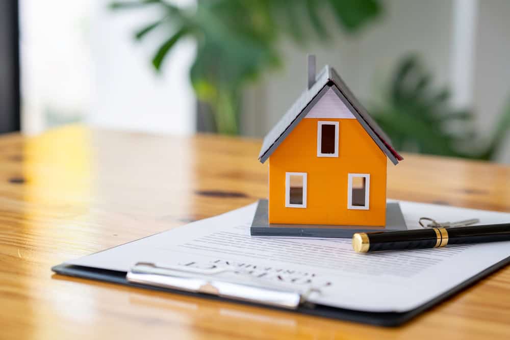 Model house on a clipboard with a pen, symbolizing home ownership and real estate transactions.