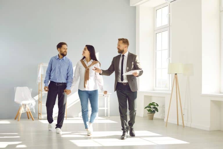 A real estate agent shows a young couple a bright, modern apartment.