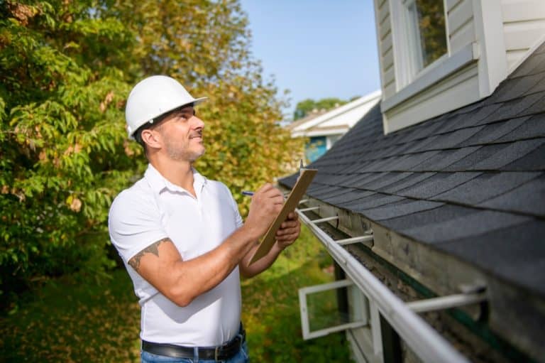 Home inspector evaluating a roof and gutters on a sunny day.