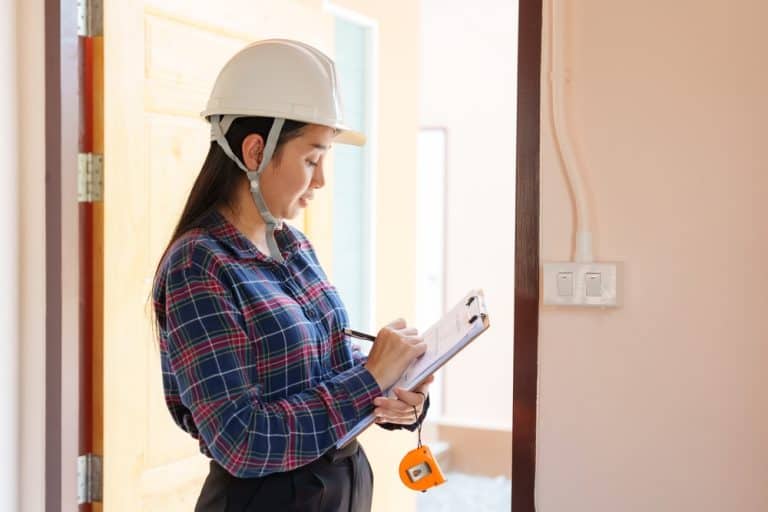 Female engineer conducting an inspection, taking notes on a clipboard inside a building.