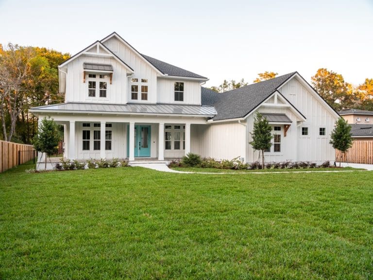Charming two-story home with a vibrant turquoise door, nestled in a lush green lawn under a serene sky.