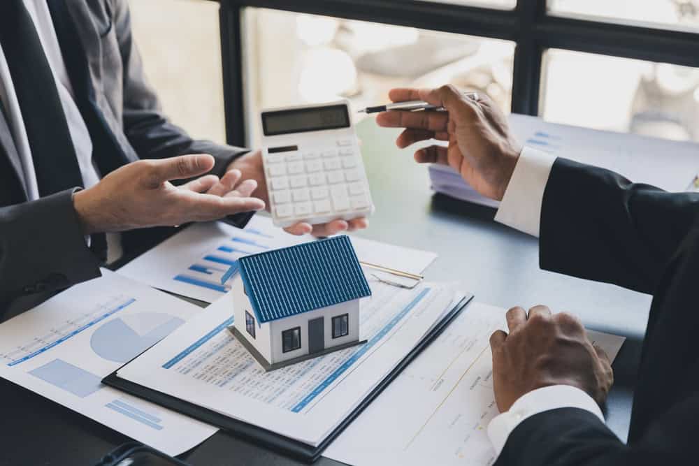 Business professionals discussing real estate investment and mortgage calculations with model house and calculator on the table.