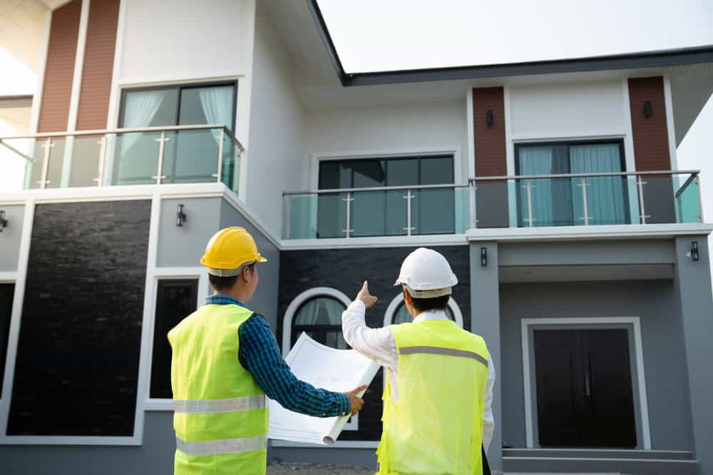 Engineers discuss plans in front of a modern two-story house under construction.