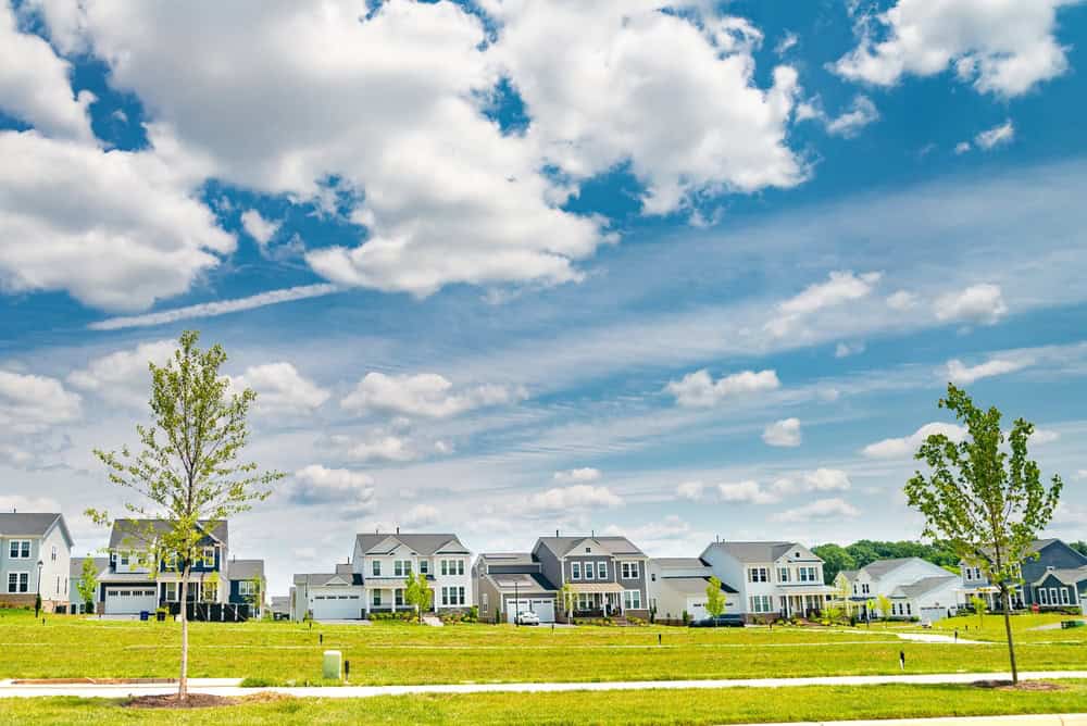 A vibrant suburban neighborhood under a bright blue sky with fluffy white clouds.