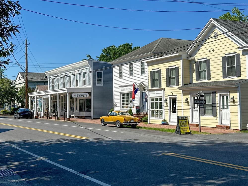 Charming small-town street with historic buildings, a vintage yellow convertible, and a cozy creamery on a sunny day.