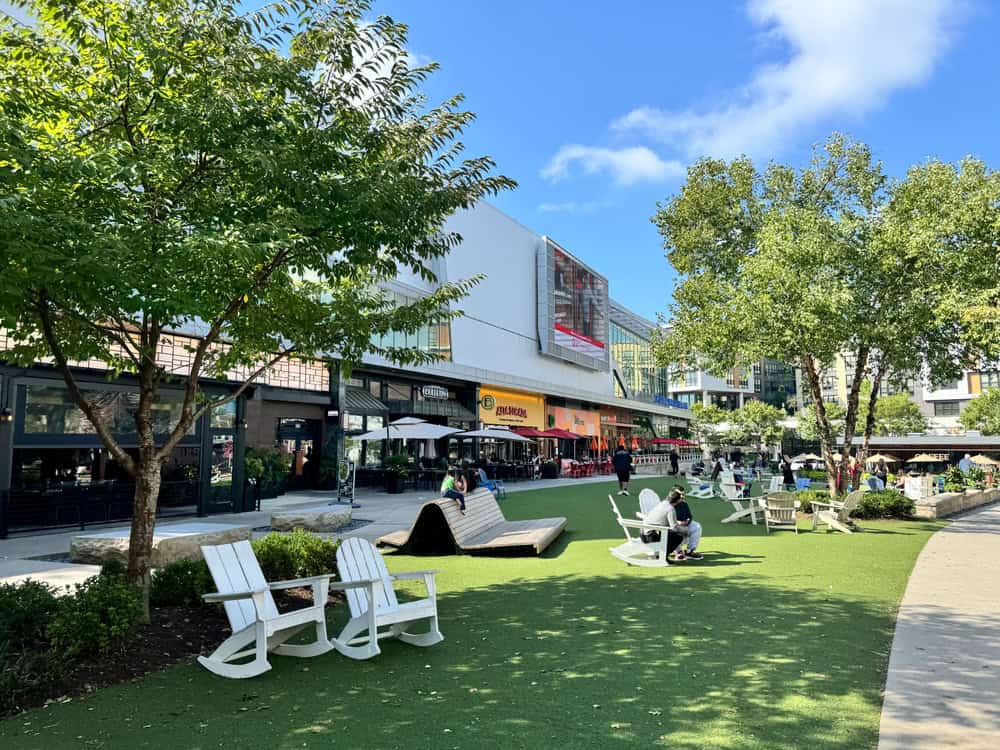 A vibrant outdoor plaza with lush greenery, cozy seating, and lively restaurants—perfect for relaxation and gathering under the sun.