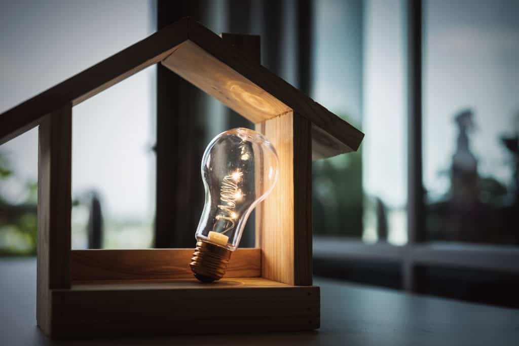 Creative home lighting concept with a glowing light bulb inside a wooden house frame, symbolizing innovation and energy efficiency.