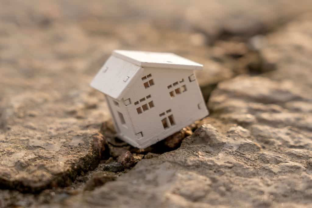 A house leaning against a crack on the ground, symbolizing instability.