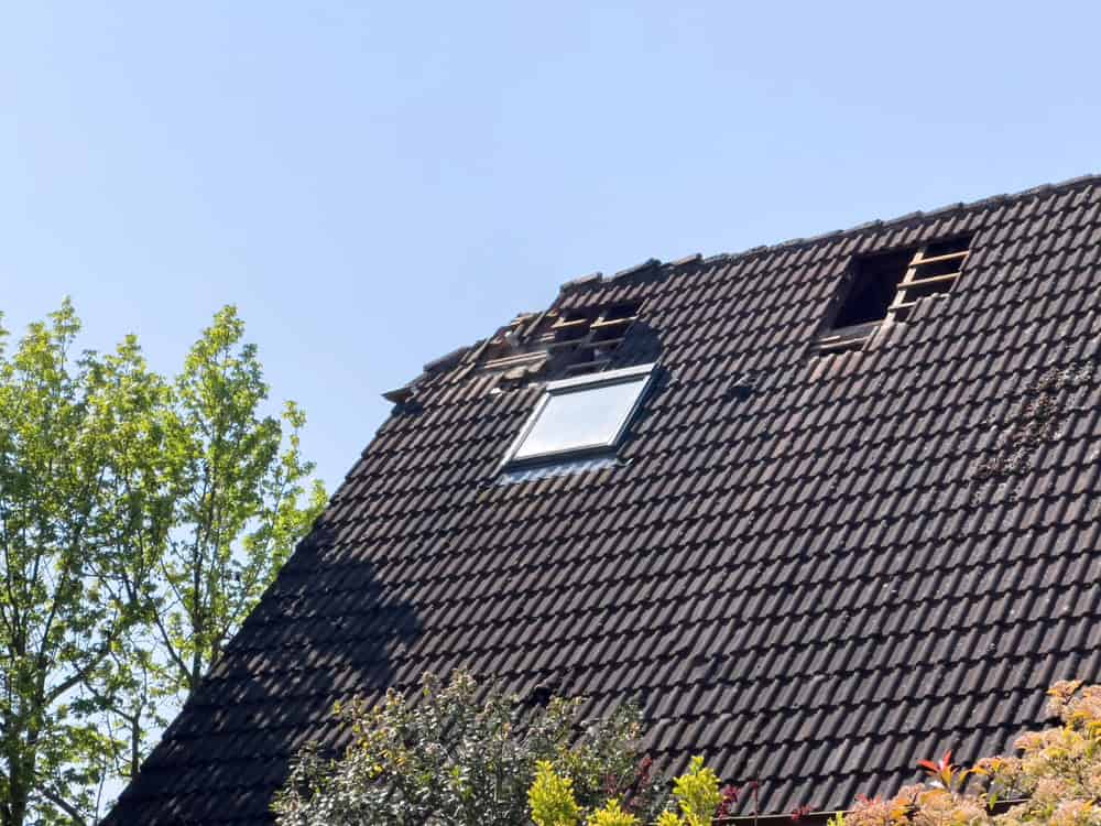 Roof damage in need of urgent repair under a clear blue sky.